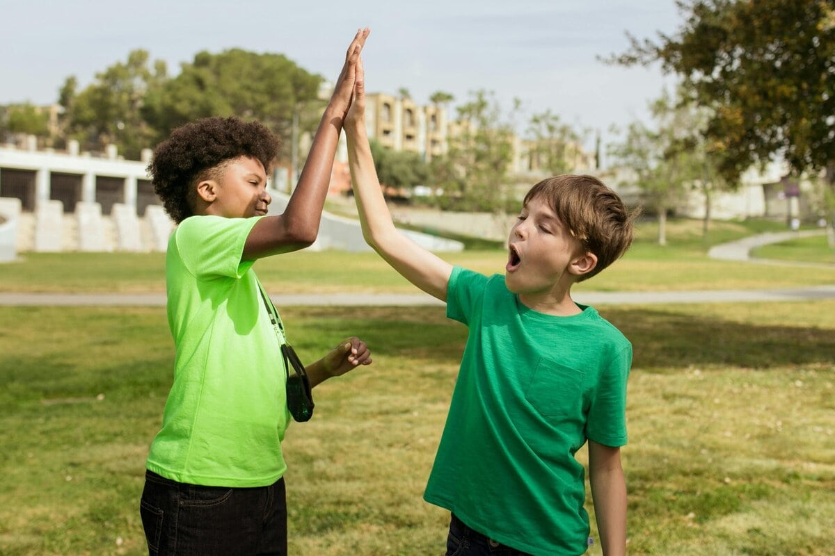 Two children high-fiving each other energetically in a sunny park setting.